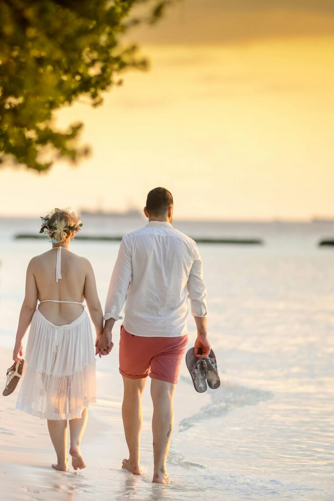 man and women walking on beach carrying their shoes